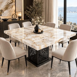 Pode incluir: Uma mesa de jantar quadrada com tampo de mármore polido bege e branco com veios castanhos, apoiada numa base de metal preto com um padrão intrincado cortado a laser, rodeada por oito cadeiras estofadas com pernas pretas afuniladas.