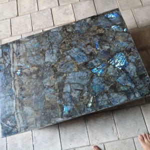 May include: A rectangular tabletop featuring a mosaic of polished labradorite stone pieces. The surface displays a deep dark gray and black base color with prominent iridescent blue and gold flashes throughout the fragmented mineral segments.