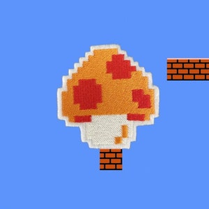 May include: A pixelated mushroom patch with an orange and red cap, white stem, and brick base, set against a blue sky background with clouds, a question mark block, and a brick platform. The design is reminiscent of a classic video game.