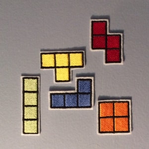 May include: Set of seven embroidered iron-on patches featuring different Tetris game pieces in various colors, including yellow, blue, red, and orange.