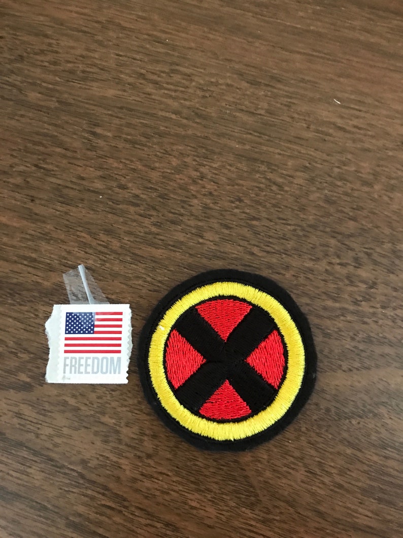 K&ouml;nnte beinhalten: Ein gestickter schwarzer, roter und gelber Aufn&auml;her mit einem X in der Mitte. Der Aufn&auml;her ist rund und hat einen gelben Rand. Der Text "FREEDOM" ist auf einem kleinen Aufkleber mit der amerikanischen Flagge im Hintergrund sichtbar.
