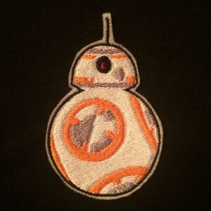 May include: A white and orange embroidered patch of a Star Wars droid, BB-8, with a black background.