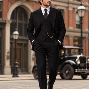 May include: A black three-piece suit consisting of a blazer, a button-up vest, and trousers, worn with a white collared shirt and a black tie. A gold pocket watch chain is attached to the vest. The text RUBY ATTIRE is visible in the top left corner.