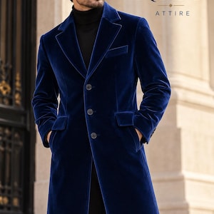 May include: A long, royal blue velvet overcoat featuring a notched lapel, three front buttons, and two flap pockets. The coat is worn over a black turtleneck sweater. The text RUBY ATTIRE is visible in the upper right corner of the image.