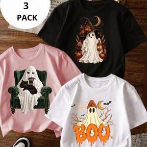 May include: A 3-pack of short-sleeve t-shirts in black, light pink, and white. The black shirt features a ghost in a witch hat with pumpkins. The pink shirt shows a ghost sitting in a green armchair with a black cat. The white shirt displays a ghost with the text BOO.