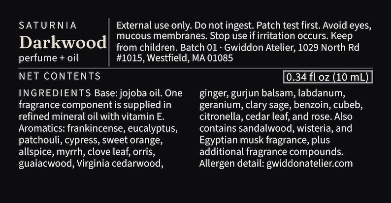 May include: A black product label for Saturnia Darkwood perfume and oil, 0.34 fl oz. Text includes safety warnings, batch 01, Gwiddon Atelier address, and a list of ingredients such as jojoba oil, frankincense, eucalyptus, patchouli, and sandalwood.