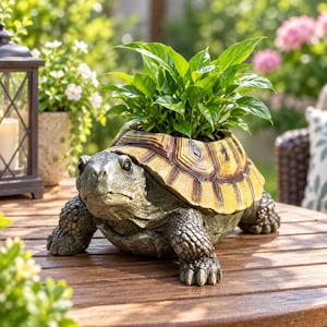 Peut inclure: Un pot de fleurs en forme de tortue avec un corps texturé gris et une carapace aux motifs jaunes et bruns. Le pot contient une plante verte aux feuilles vives, avec la tête et les quatre pattes de la tortue visibles sur une surface en bois.