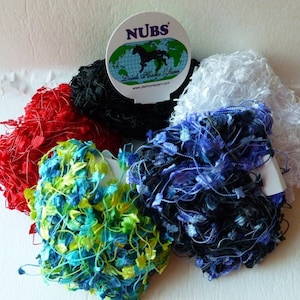 May include: Five balls of yarn in different colors, including red, black, blue, green, and white. The yarn is a fluffy, textured type. A label with the text "NUBS" and a logo of a horse on a globe is visible.