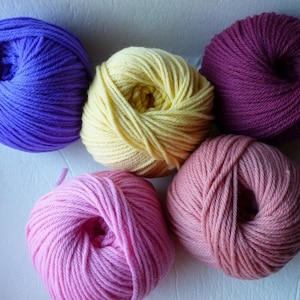 May include: Five skeins of yarn in various colors: purple, yellow, deep purple, pink, and peach. The yarn is tightly wound into round balls, perfect for knitting or crocheting projects. The colors are vibrant and appealing.