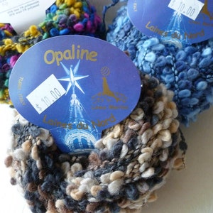 May include: Three balls of yarn in different colors: blue, brown and beige, and green, yellow, and pink. Each ball has a price tag attached with the price of $10.00. The yarn is labeled "Opaline" and "Laine du Nord".