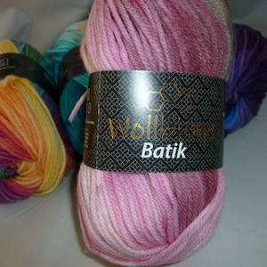 May include: Three skeins of yarn in different colors. The skein in the center is pink and white with a label that reads "Wollzwiebel Batik". The skein on the left is a rainbow of colors. The skein on the right is purple and blue.