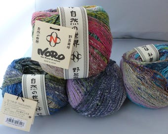 May include: Four skeins of Noro yarn in various colors, including pink, blue, purple, and green. Each skein is labeled with Japanese text and a tag that reads "Noro, the World of Nature, Made in Japan."