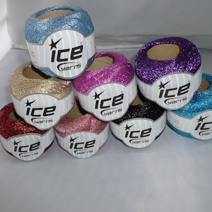 May include: A collection of colorful glitter yarn balls in shades of blue, gold, pink, purple, red, and black. Each ball has a label that reads "ice yarns". The yarn is arranged in a stacked formation.