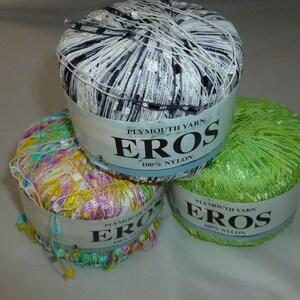 May include: Three spools of Plymouth Yarn Eros 100% nylon yarn. The spools are in black and white, pink and green, and green. Each spool has a label with the brand name and yarn type.
