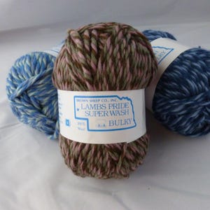 May include: Three skeins of yarn in different color combinations. The skein in the center is brown, pink, and green. The label reads "Lambs Pride Superwash Bulky" and "Brown Sheep Co., Inc.".