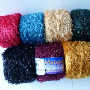 May include: Eight skeins of sparkly yarn in various colors, including red, teal, beige, green, black, burgundy, and gold. The yarn is labeled "Mango Sparkle 70% Nylon, 30%".