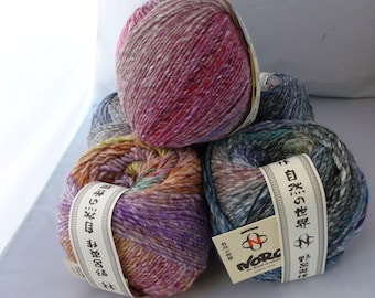 May include: A collection of four round balls of variegated yarn in shades of pink, purple, orange, blue, and grey. Each ball features a paper band with the text Noro, the Works of Nature, and Japanese characters, indicating a multi-colored fiber.