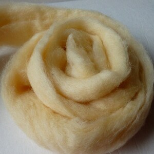 May include: A close-up of a light yellow, fluffy ball of wool yarn. The yarn is rolled into a spiral shape.