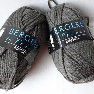 May include: Two skeins of gray yarn with black labels. The labels read "BERGERE de France MAGIC+". The yarn is a solid gray color and appears to be a medium weight. The skeins are ready for knitting or crocheting projects.