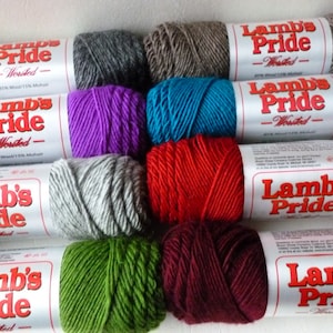 May include: A collection of ten skeins of Lamb's Pride worsted weight yarn in various colors, including gray, purple, teal, red, green, and burgundy.