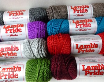 May include: A collection of eight skeins of Lamb's Pride Worsted yarn in various colors including charcoal, brown, purple, teal, light gray, bright red, olive green, and deep burgundy, each featuring a white label with red text and fiber content.