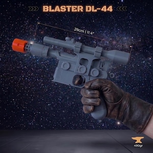 Op de afbeelding: Een grijs DL-44 blaster speelgoed met een feloranje mondingspunt en een gemonteerde richtkijker. De blaster is 29 cm lang en weegt 490 gram. Het ontwerp is voorzien van een getextureerde handgreep en cirkelvormige details aan de zijkant.