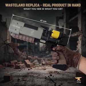 Puede incluir: Una réplica de arma de utilería que mide 41 cm de largo y pesa 400g. El dispositivo presenta un cañón gris, una sección de agarre marrón estriada, un marco negro y un componente cilíndrico amarillo. El texto dice: WASTELAND REPLICA.