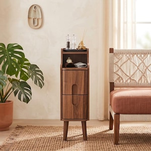 May include: A tall, narrow dark wood nightstand featuring two stacked drawers with vertical recessed handles and an open top shelf. The unit stands on four tapered legs and holds a small tray with two glass shakers and a reed diffuser on top.