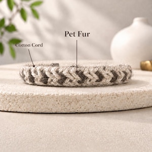 May include: A braided bracelet featuring a combination of light-colored cotton cord and dark-colored pet fur. The design displays a repeating chevron pattern throughout the band, with text labels pointing to the cotton cord and pet fur components.