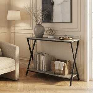 Puede incluir: Una mesa consola rectangular con tablero gris claro y base de metal negro en forma de X. La mesa cuenta con un estante inferior que sostiene una fila de libros y una cesta de mimbre tejida con un paño blanco. Un jarrón gris con ramas encima.
