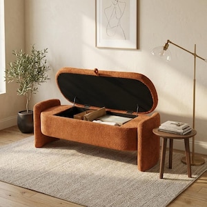 Peut inclure: Un banc de rangement de forme ovale recouvert d'un tissu texturé couleur rouille. Le couvercle à charnière est ouvert, révélant un compartiment intérieur creux. Le banc présente des bords arrondis et des supports latéraux robustes.