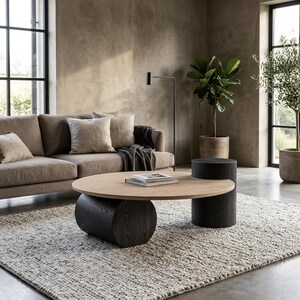 May include: A round coffee table featuring a light wood top supported by two cylindrical black wooden bases of different heights, with a small stack of books placed on the surface of the table.