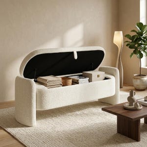 Peut inclure: Un banc de rangement en bouclé texturé blanc cassé avec une silhouette incurvée et allongée. Le couvercle à charnière est ouvert, révélant une doublure intérieure noire et un compartiment contenant des textiles pliés, un panier et une boîte.