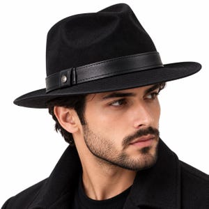 May include: A black fedora hat featuring a structured crown and a wide brim. The hat is accented with a smooth black leather band that wraps around the base, secured by a small metallic stud detail on the side, creating a clean and uniform look.