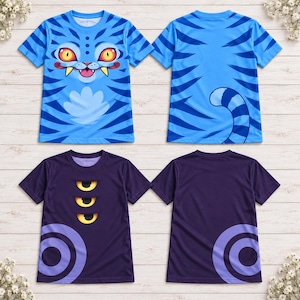 May include: Two short-sleeve t-shirts. The first is light blue with dark blue tiger stripes, a cartoon cat face with yellow eyes and fangs on the front, and a tail on the back. The second is dark purple with three yellow eyes and purple circles.