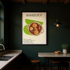 Pode incluir: Uma impressão artística emoldurada intitulada SIMMER POT com um gráfico de uma panela cheia de fatias de laranja e especiarias sobre uma forma verde abstrata. O texto lista ingredientes: 2 laranjas sanguíneas, 1 maçã vermelha, 5 paus de canela, 4 anis estrelados e 1 colher de sopa de extrato de baunilha.