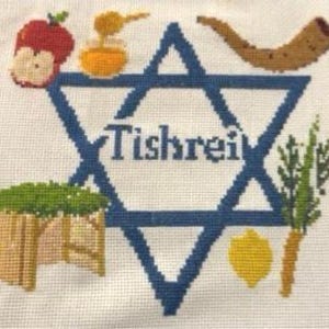 Pode incluir: Um bordado em ponto cruz sobre tecido branco apresentando uma grande Estrela de Davi azul com a palavra Tishrei no centro. Ao redor da estrela estão ícones bordados, incluindo uma maçã vermelha, mel, um shofar, uma sucá, um etrog amarelo e um lulav.