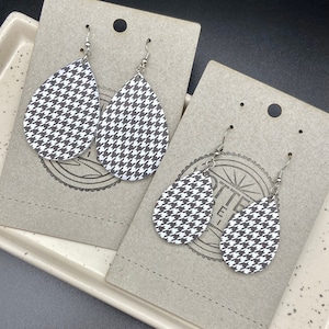May include: A pair of black and white houndstooth teardrop-shaped earrings with silver hooks.
