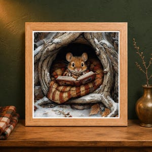 May include: A framed diamond painting featuring a brown mouse sitting inside a hollow tree trunk, wrapped in a brown and orange striped blanket while reading an open book. The scene includes snowy ground and fallen leaves within the tree cavity.