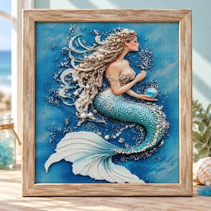 May include: A framed diamond painting featuring a mermaid with long, flowing hair adorned with white pearls. The mermaid has a teal, scale-textured tail and holds a small, glowing blue orb. The background is a textured blue gradient.