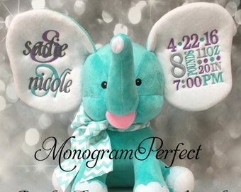 May include: A turquoise plush elephant with white ears and a pink mouth. The ears are embroidered with the text "Sadie & Nicole" and "4-22-16 8 pounds 11oz 20 in 7:00 PM". The elephant is wearing a white and green chevron scarf. The text "Monogram Perfect Birth Announcement Keepsake" is printed below the elephant.