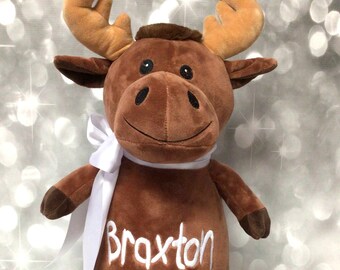 May include: Brown plush moose with white antlers and a white ribbon around its neck. The moose is embroidered with the name "Braxton".