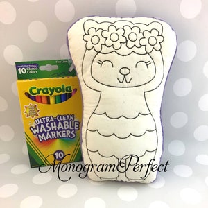 May include: A white plush toy shaped like a cat with a flower crown. The toy is outlined in black and ready to be colored. A box of 10 Crayola Ultra-Clean Washable Markers is included.