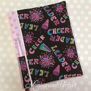 May include: A black and pink fabric pencil case with a zipper closure. The fabric has a pattern of cheerleading pom-poms, megaphones, and the words "Cheer Leader".