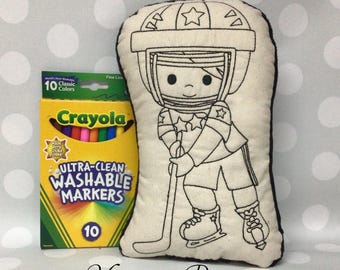 May include: A cream-colored hockey player pillow with black stitched outlines, holding a hockey stick. A box of Crayola Ultra-Clean Washable Markers with 10 classic colors is next to the pillow. The text "Monogram Perfect" is at the bottom.