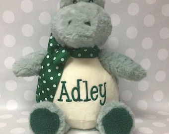 May include: A plush stuffed alligator toy with soft sage green fur, dark green textured foot pads, and a dark green scarf featuring white polka dots. The alligator has a cream-colored belly embroidered with the name Adley in dark green script.