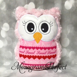 May include: A pink plush owl toy with a white face, large black eyes, and an orange beak. The owl's chest has a pink heart pattern with the words "Kiss Me Sweet" and "Be Mine". The text "Monogram Perfect" is at the bottom.