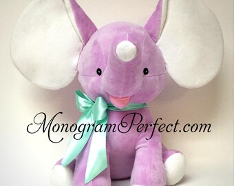 May include: A plush elephant toy in a light purple color with large white inner ears, white feet, and a white tip on its trunk. The elephant features a mint green satin ribbon tied in a bow around its neck and the text MonogramPerfect.com.