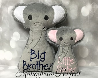 May include: Two gray plush elephant toys with embroidered details. The larger elephant has "Big Brother" embroidered on it in blue thread. The smaller elephant has "Little Sister" embroidered on it in pink thread. The text "Monogram Perfect" is also embroidered on the bottom of the image.