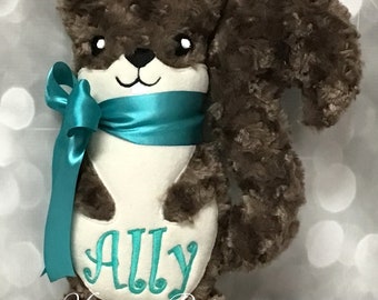 May include: A brown plush squirrel with a white belly and a teal blue ribbon around its neck. The squirrel has a white face with black eyes and a black nose. The squirrel is embroidered with the name "ALLY" in teal blue thread. The text "Monogram Perfect" is also embroidered on the squirrel's belly.